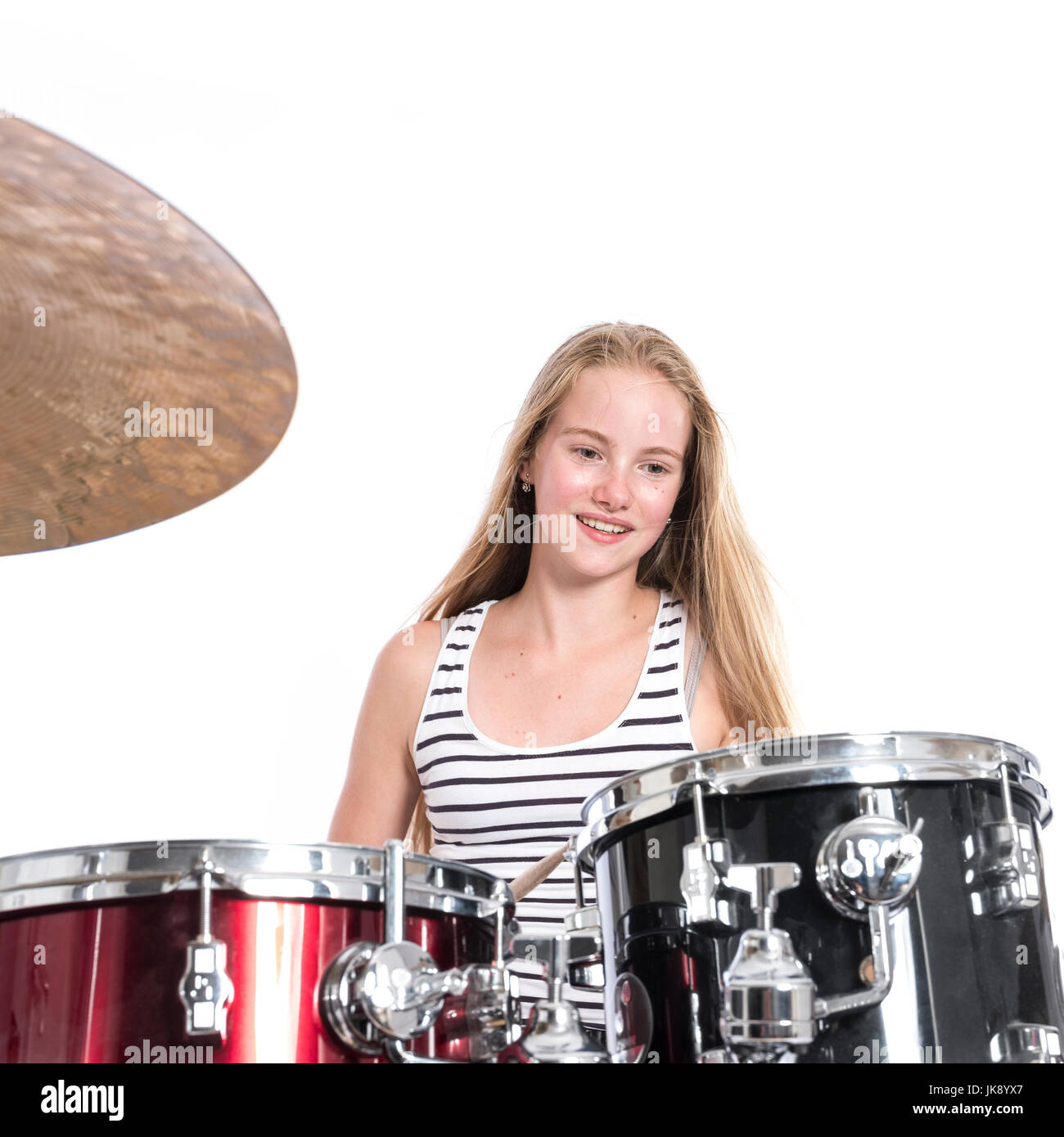 young blond caucasian teenage girl plays the drums in studio against white background Stock Photo