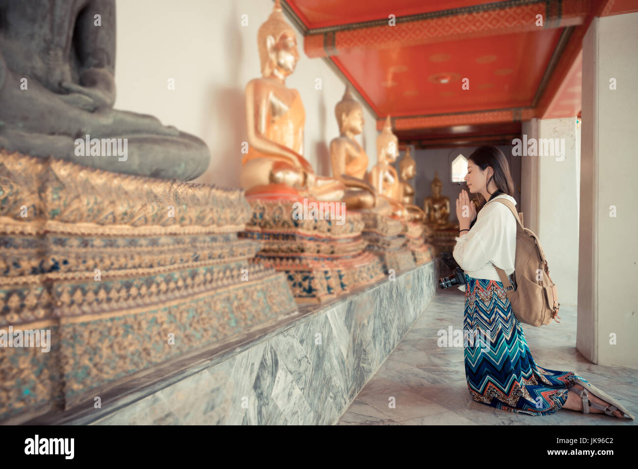 elegance smiling female tourist kneel down in Bangkok famous wat pho temple and praying with buddha with vintage retro film color style on Thailand tr Stock Photo