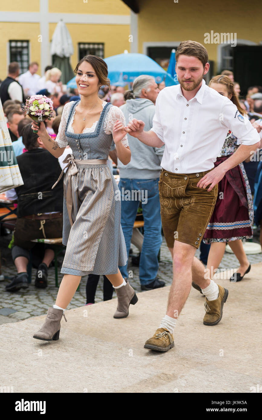 Young Bavarian couple in traditional dirndl dress and leather trousers performing traditional folk dance Bandltanz around the maypole Stock Photo