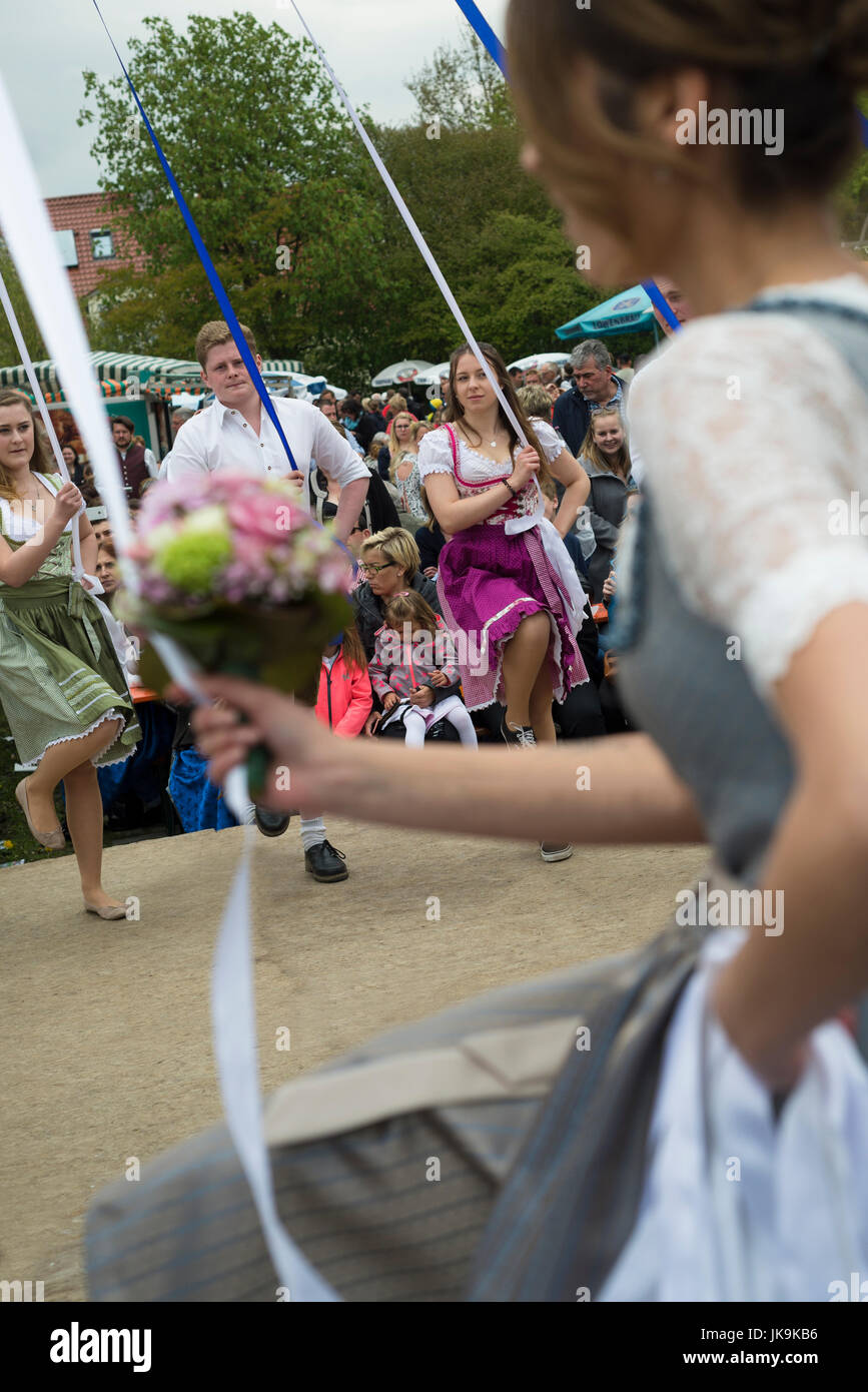 Young Bavarian men and women in traditional dresses holding ribbons while performing traditional folk dance Bandltanz around the maypole Stock Photo
