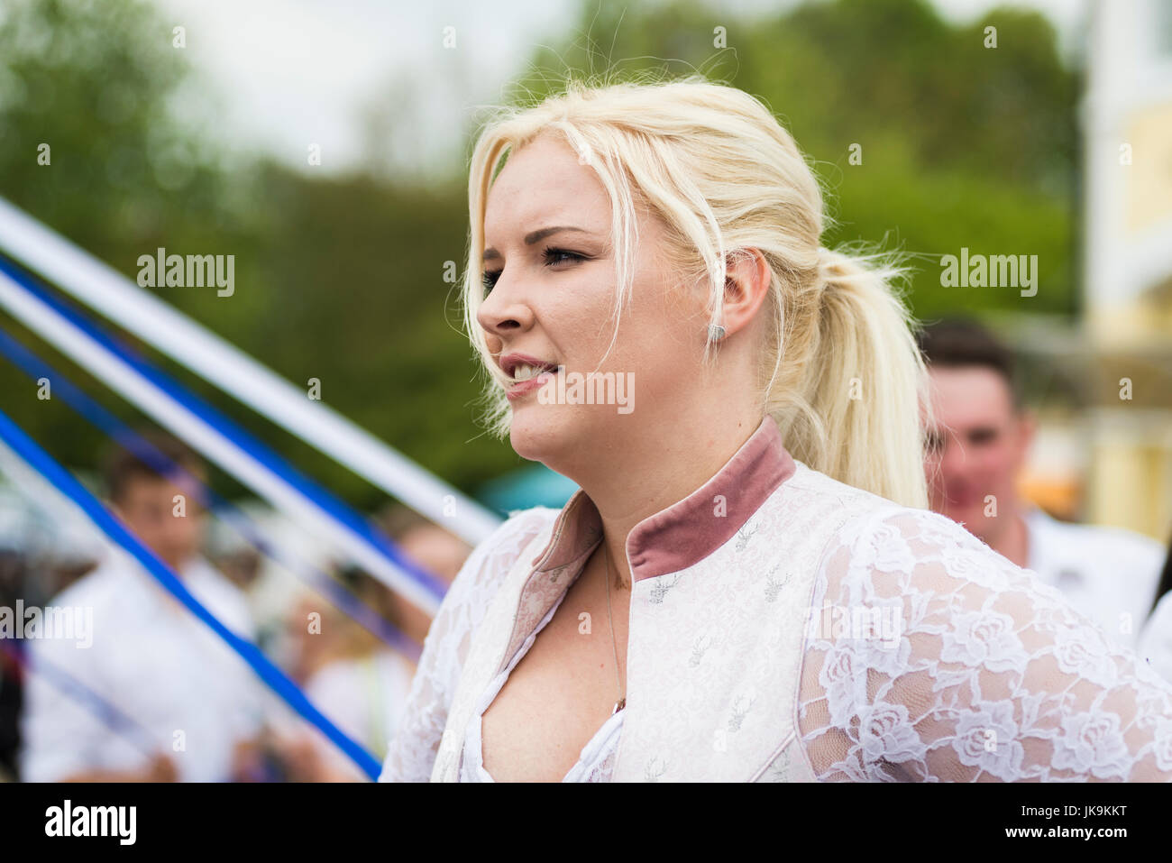 Young woman smiling while dancing a traditional Bavarian folk dance around a maypole wearing traditional dirndl dress Stock Photo