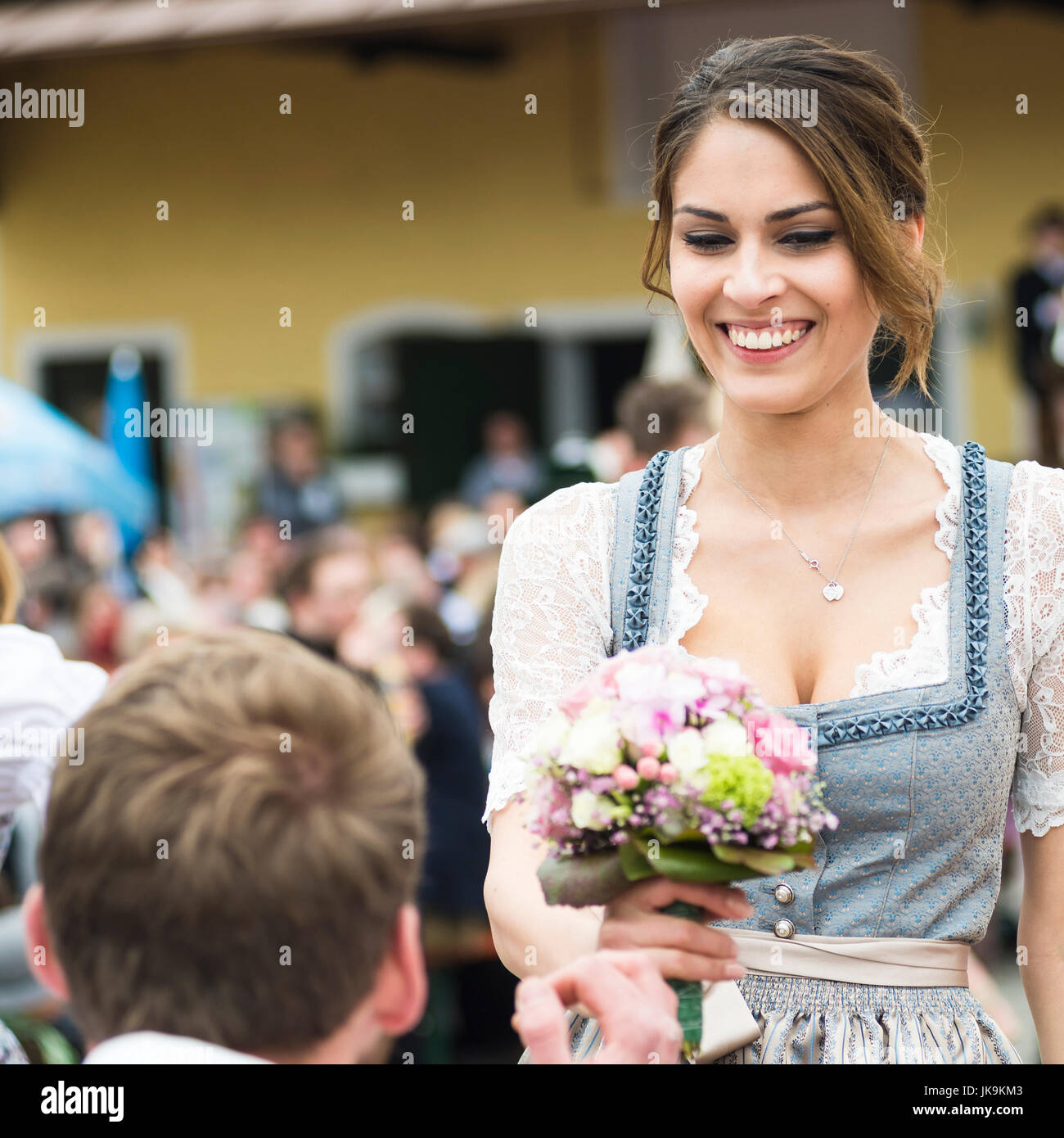 Portrait of a young man kneeling in front of a woman with a bouquet of flowers dancing a traditional Bavarian folk dance around a maypole Stock Photo