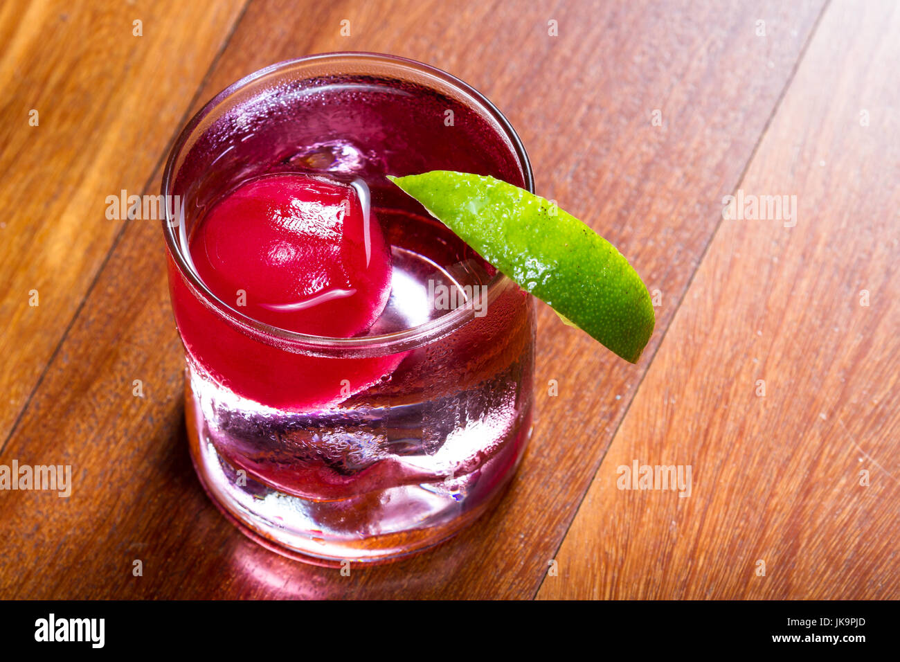 refreshing drink with a red ice ball releasing flavor into the cocktail as  it melts and chills the beverage garnished with a lime wedge on the rim of  Stock Photo - Alamy