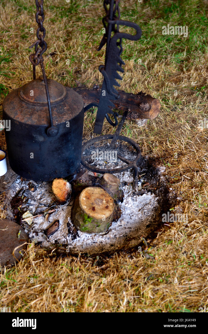 Black cast iron cooking pot hanging over wood burning campfire Stock Photo