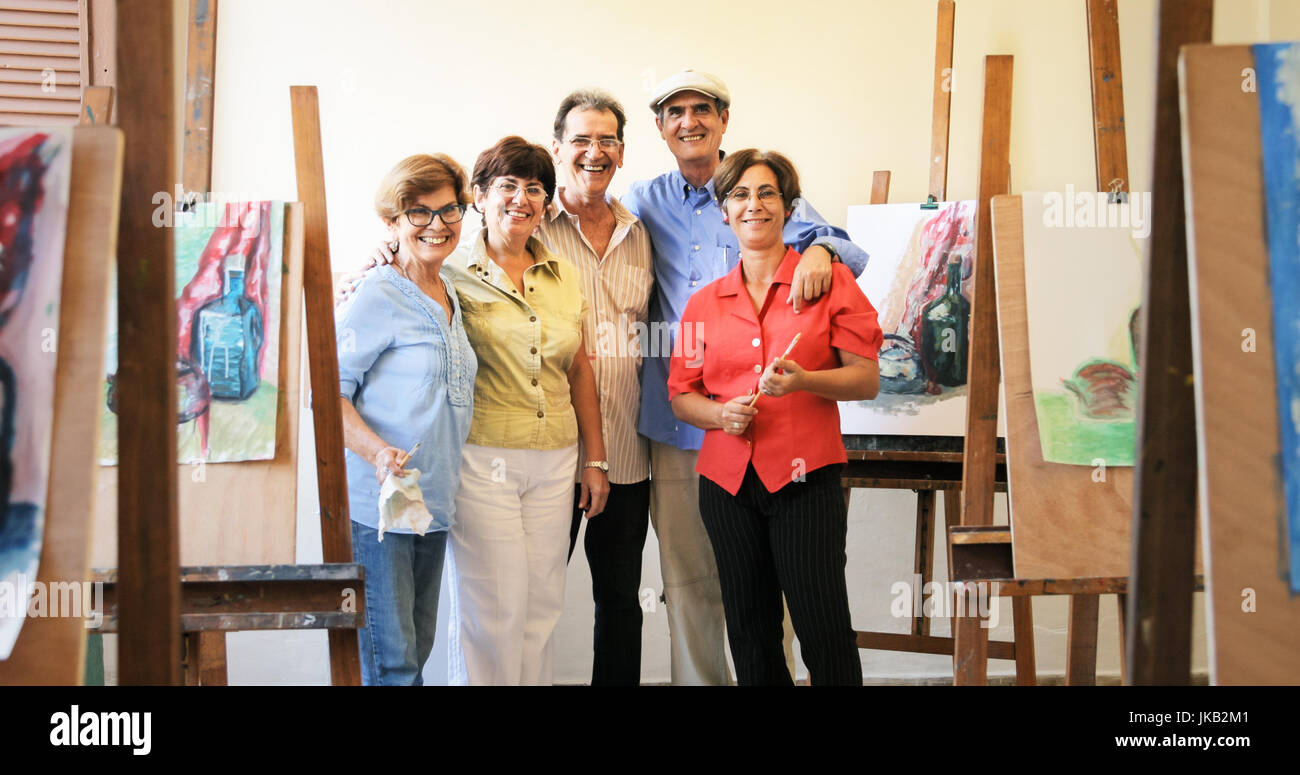 Elderly people painting for hobby. Group of active seniors at art school. Portrait of happy group of old friends with senior teacher smiling, looking  Stock Photo