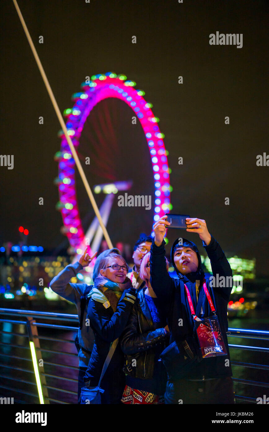 England, London, Southbank, The London Eye with tourists photographing a selfie, evening Stock Photo