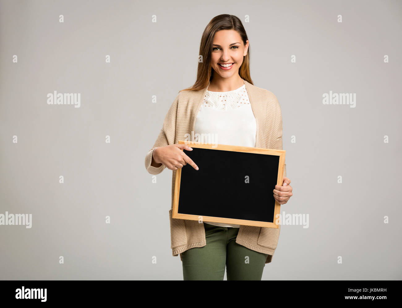 Beautiful and happy woman holding and pointing to a chalkboard Stock Photo