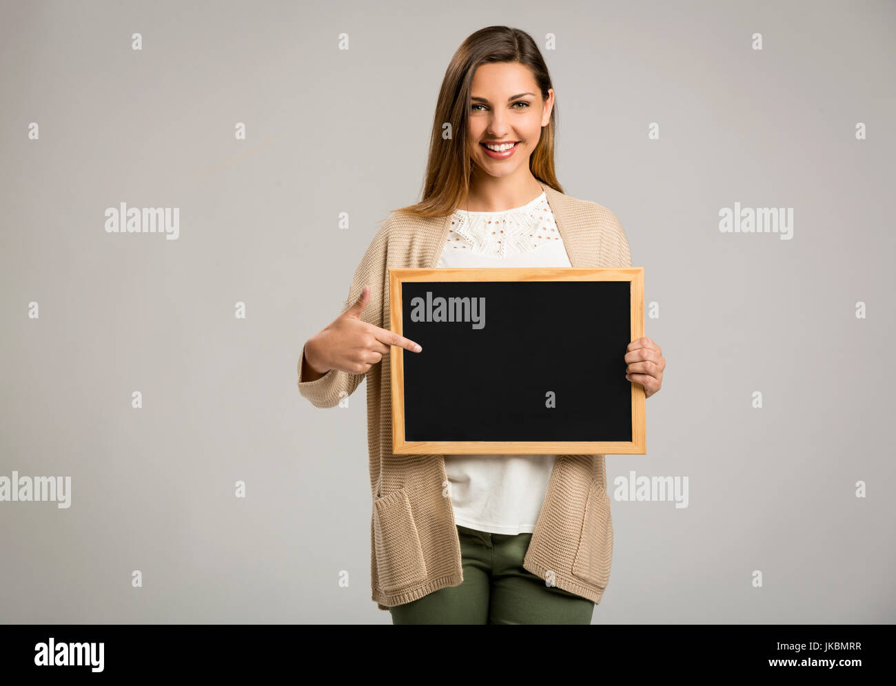 Beautiful and happy woman holding and pointing to a chalkboard Stock Photo