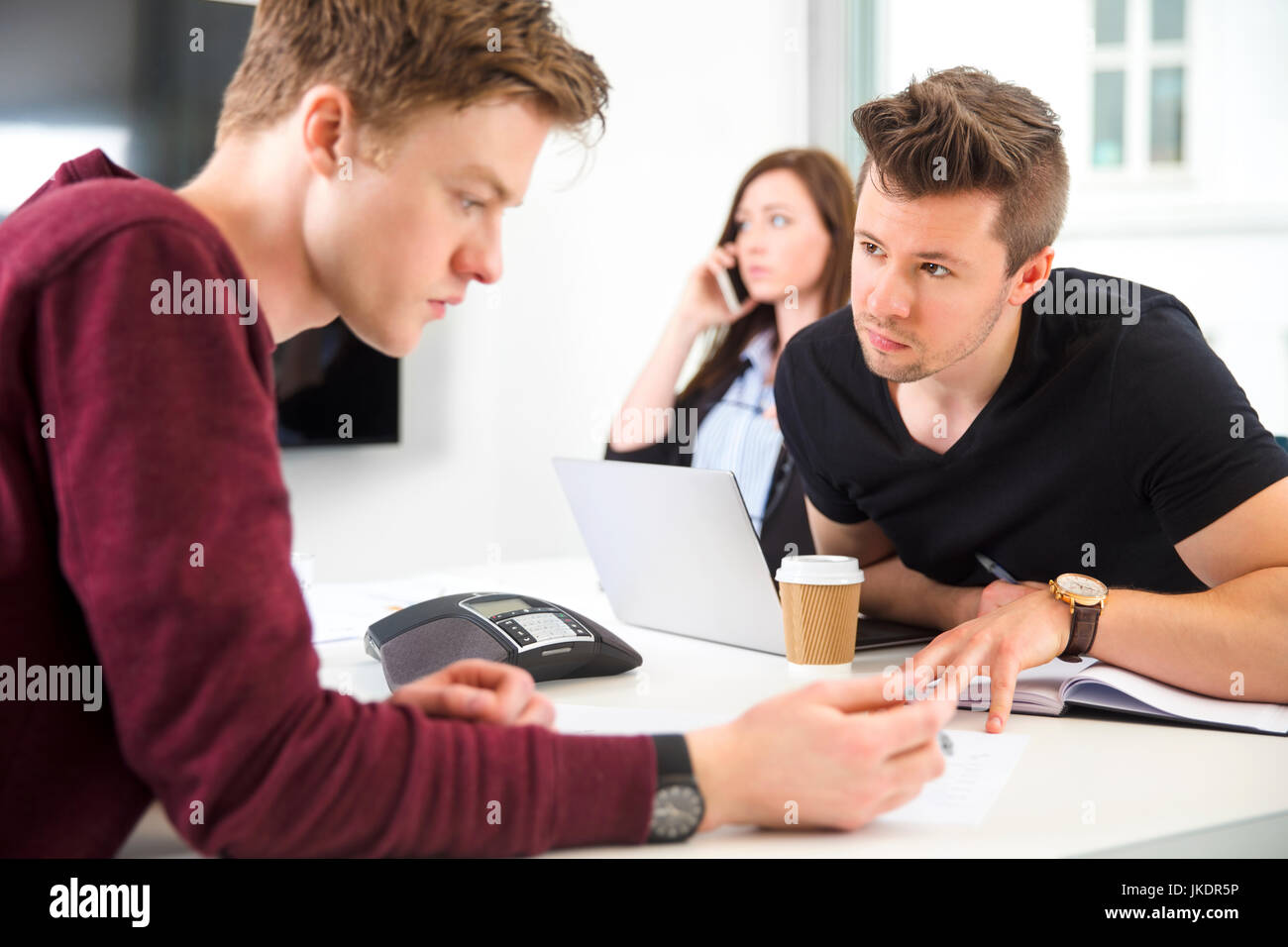 Businessmen Communicating While Colleague Using Smart Phone Stock Photo