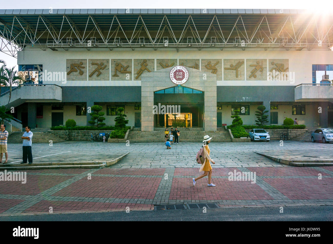 Shenzhen University building (gymnasium) with sunburst as student walks in foreground, Guangdong province, China Stock Photo