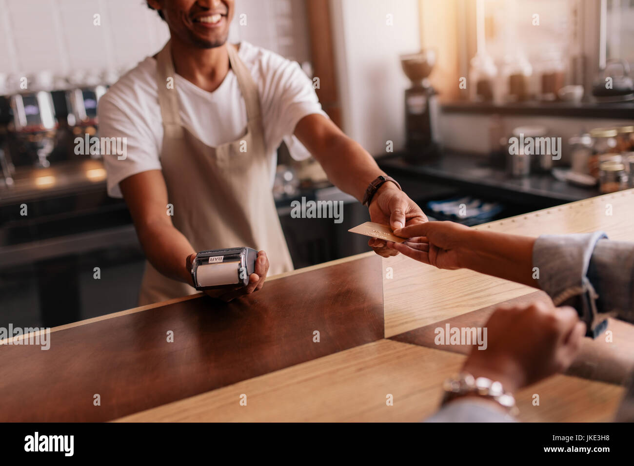 Cropped shot of customer giving credit card to male barista at cafe checkout counter. Customer paying through credit card at coffee shop. Stock Photo