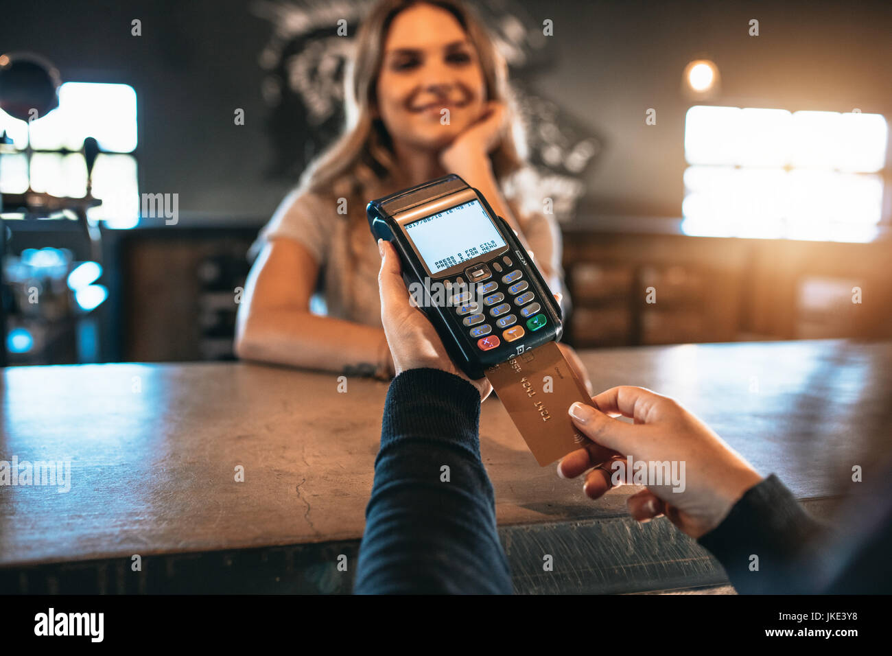 Cropped image of man paying using a credit card at bar with female behind the counter. Cashless payment at the bar. Stock Photo