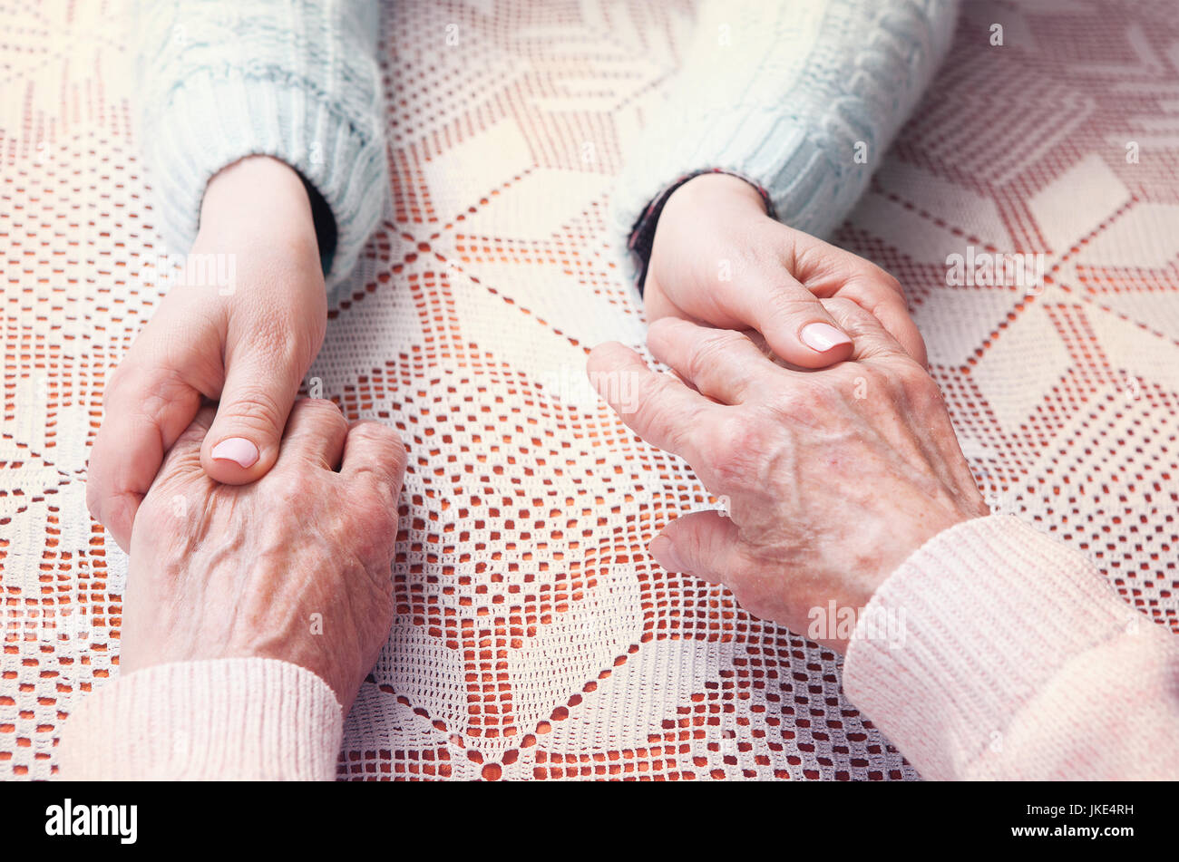 Senior woman with her caregiver at home. Holding hands, horizontally top view closeup. Stock Photo