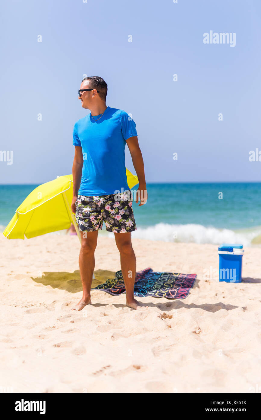 A man carrying a green umbrella and standing on the beach looking on the beach. Summer time Stock Photo