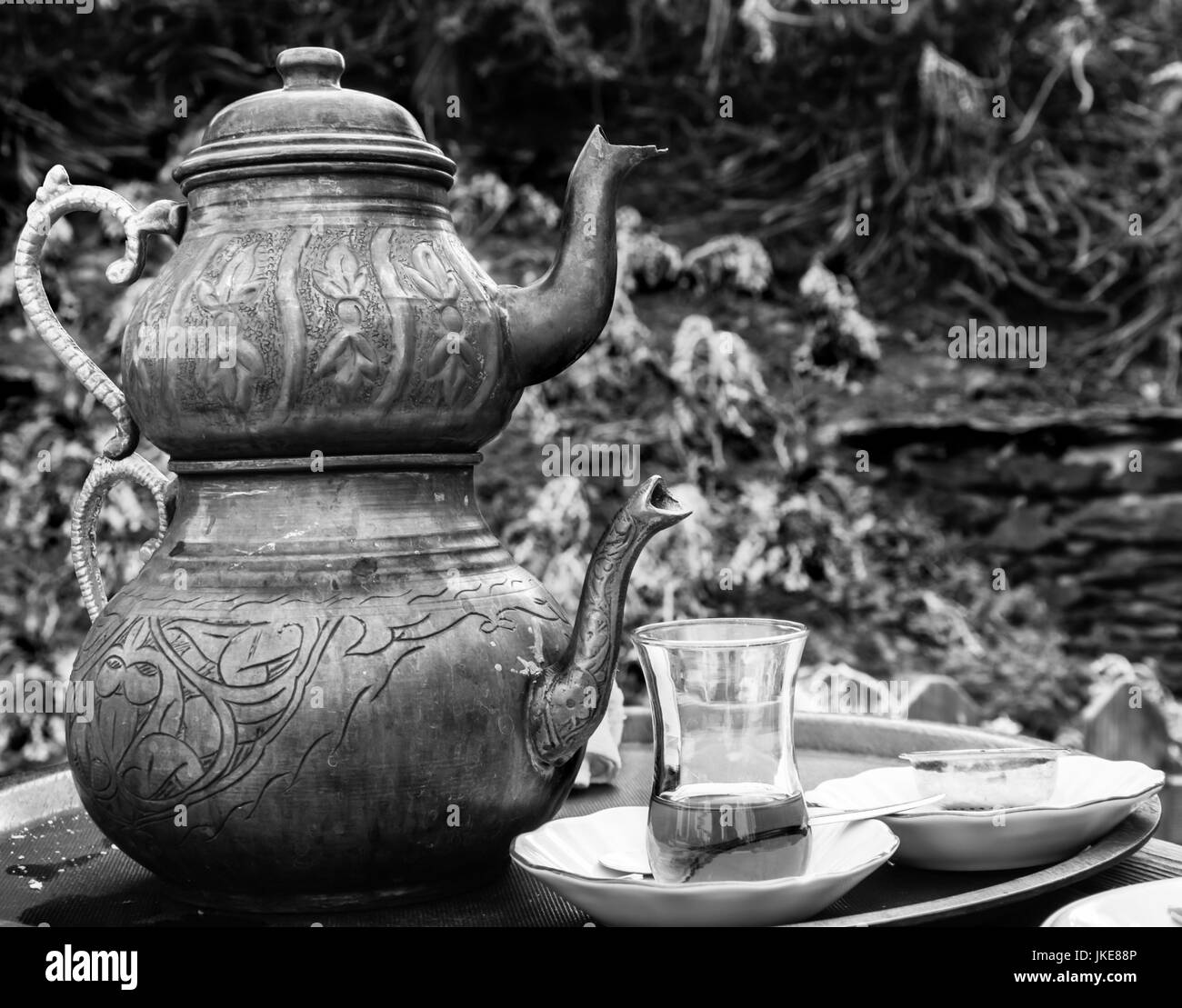 Two vintage engraved copper Turkish teapots with double stacked kettles allowing tea to be brewed, with one glass cup filled with tea, served outdoors Stock Photo