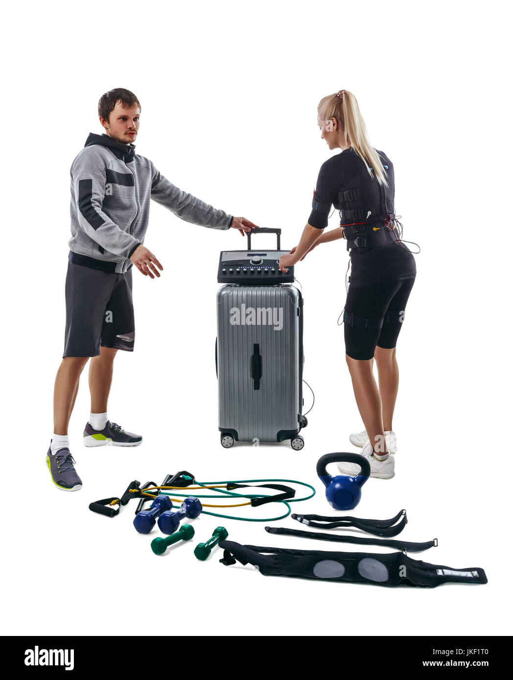 Blonde fitness woman in full electrical muscular stimulation suit and her trainer setting parameters of EMS station. Various sport gear like kettlebel Stock Photo