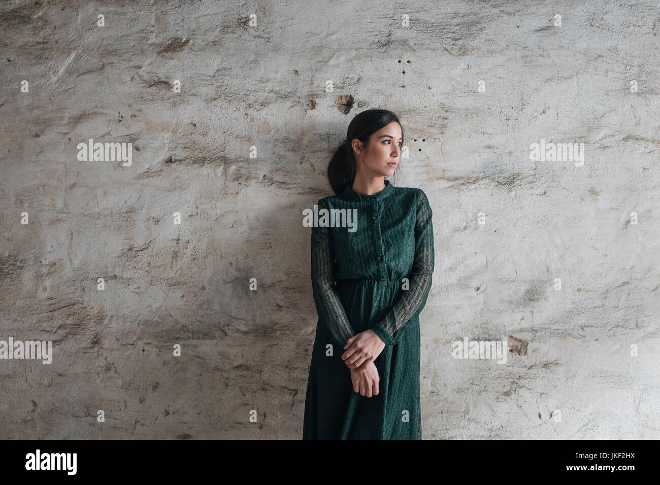 Young woman wearing green dress, staning in front of wall Stock Photo ...