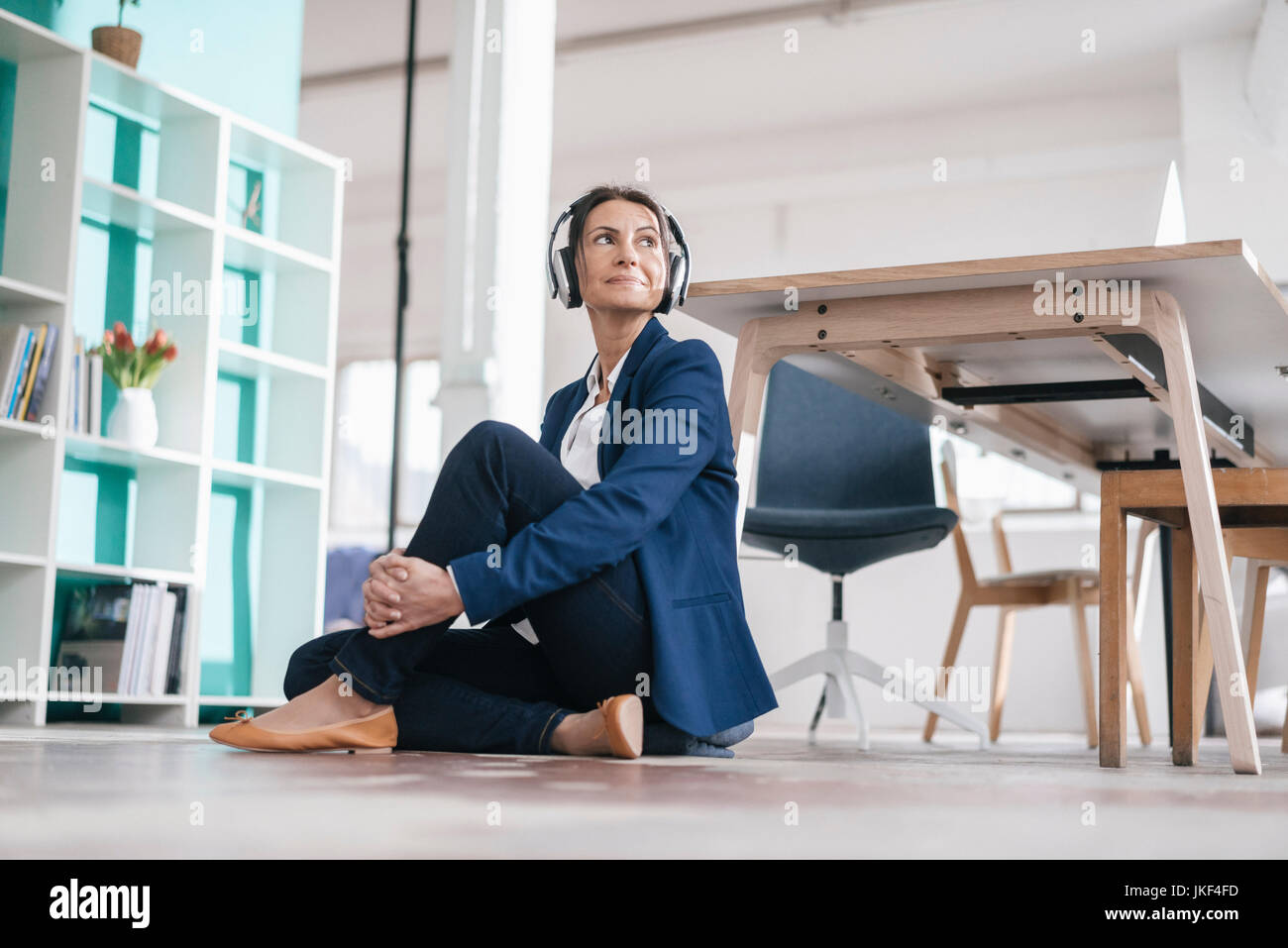 Businesswoman sitting on the floor in a loft listening music with ...