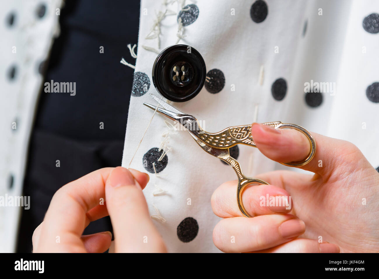 Woman's hands stitching button on a dress, close-up Stock Photo