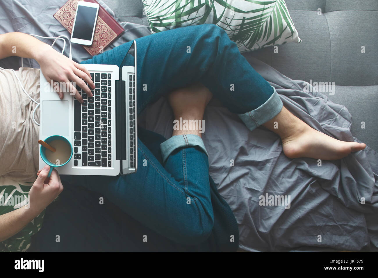 Man using laptop and drinking coffee on sofa bed, partial view Stock Photo