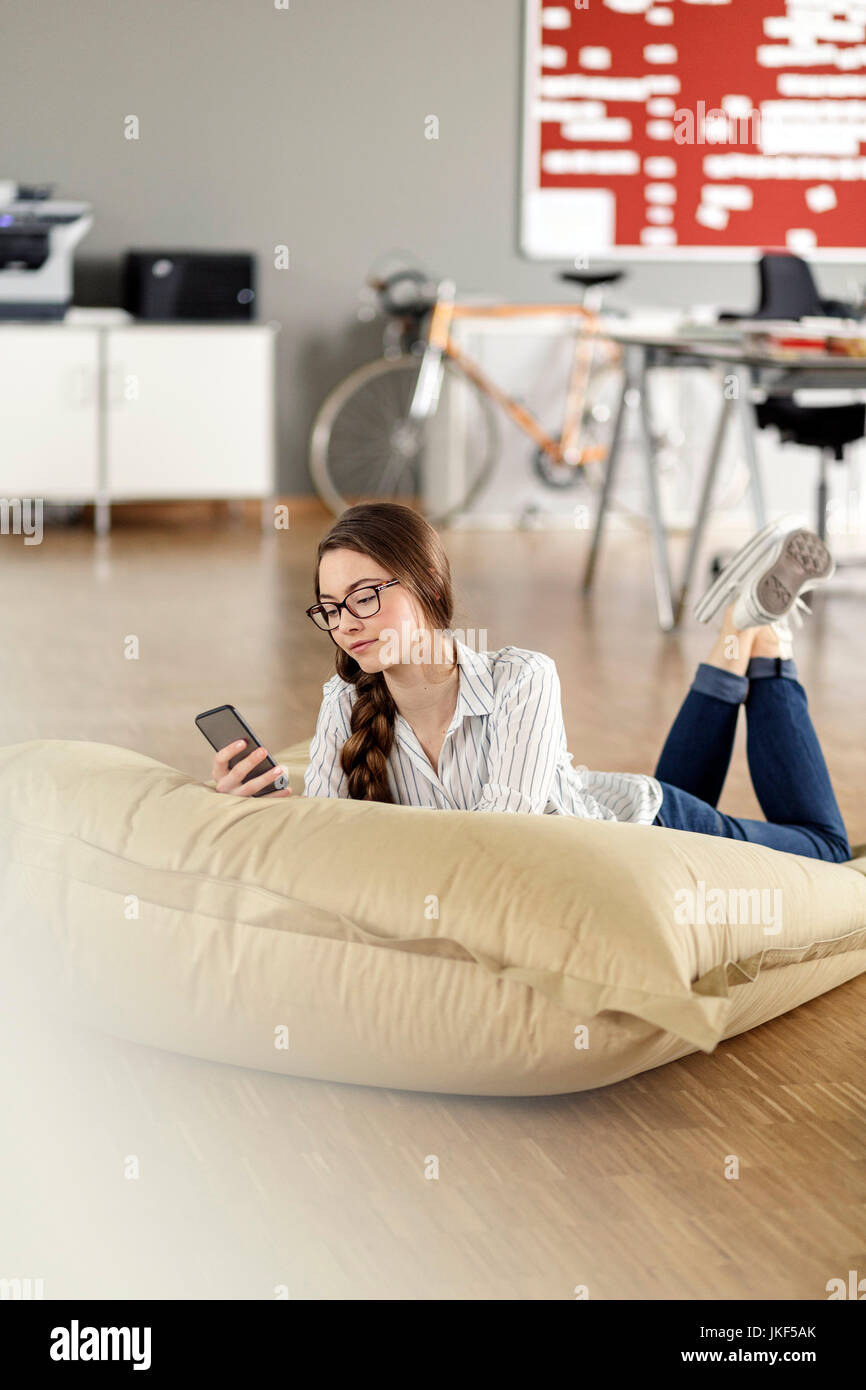 Young woman with cell phone lying in bean bag in office Stock Photo - Alamy