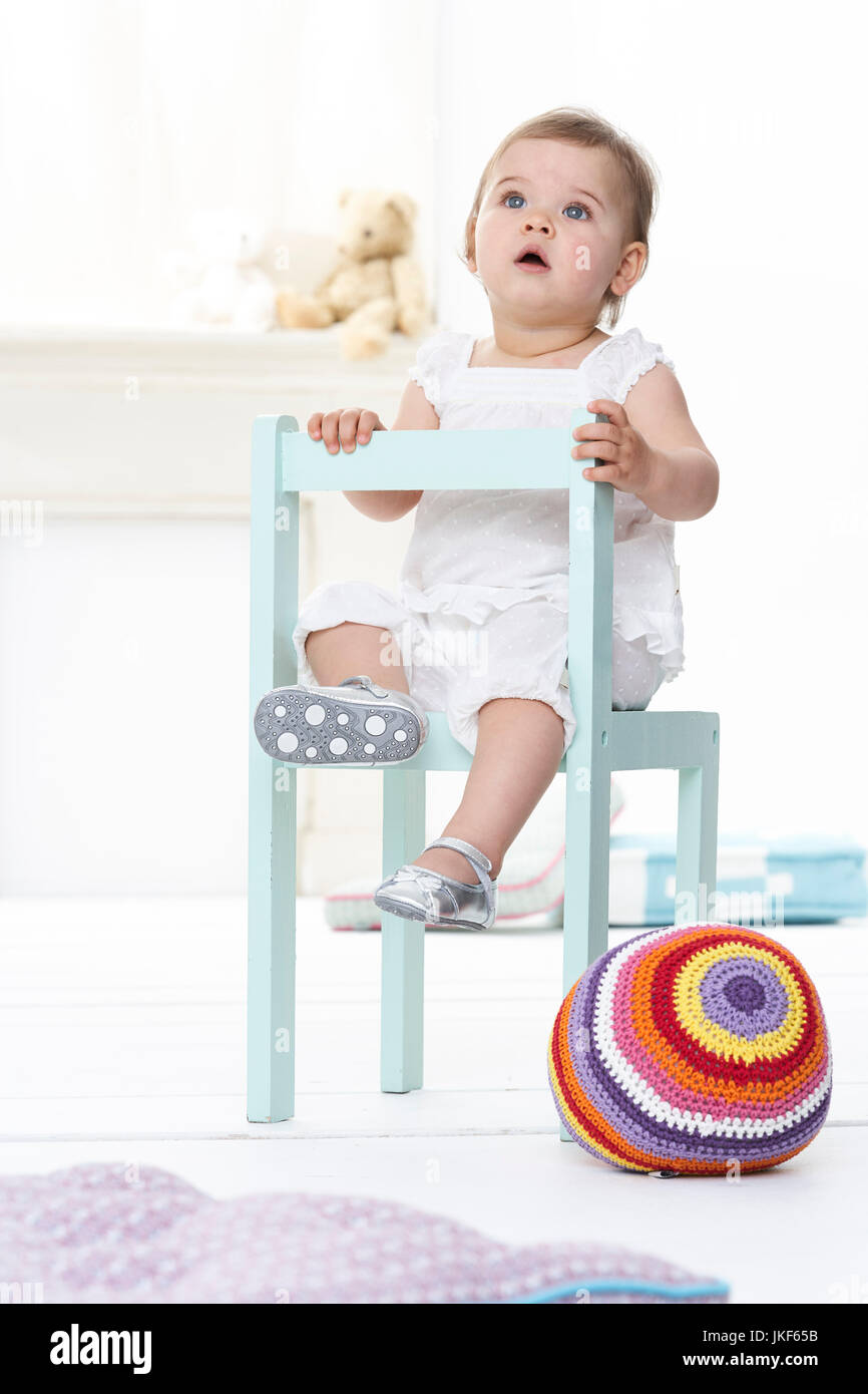 Portrait of baby girl sitting on chair looking up Stock Photo - Alamy