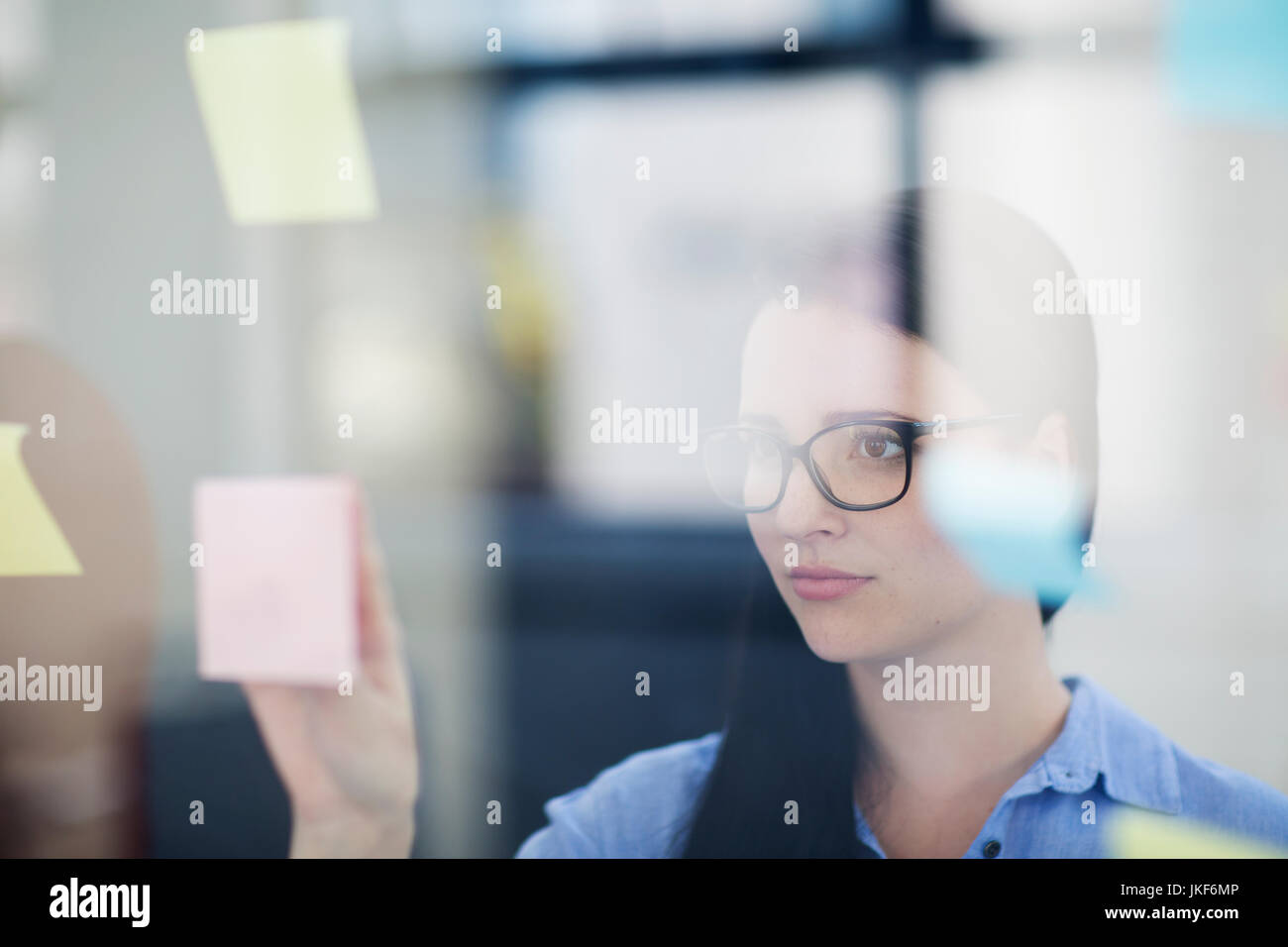 Female employee placing sticky notes on glass Stock Photo