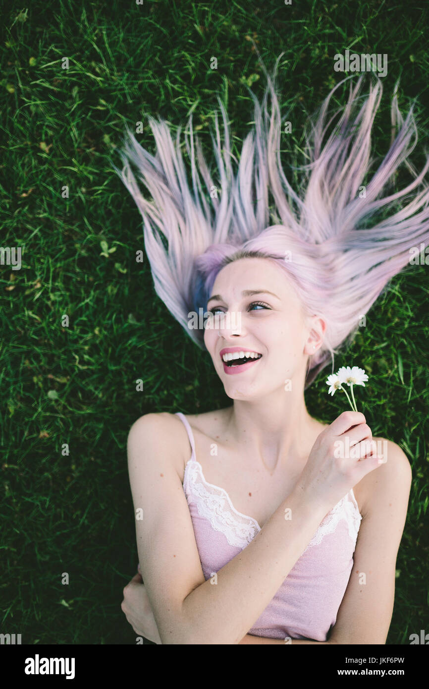Portrait of laughing woman lying on grass with eyes closed holding ...