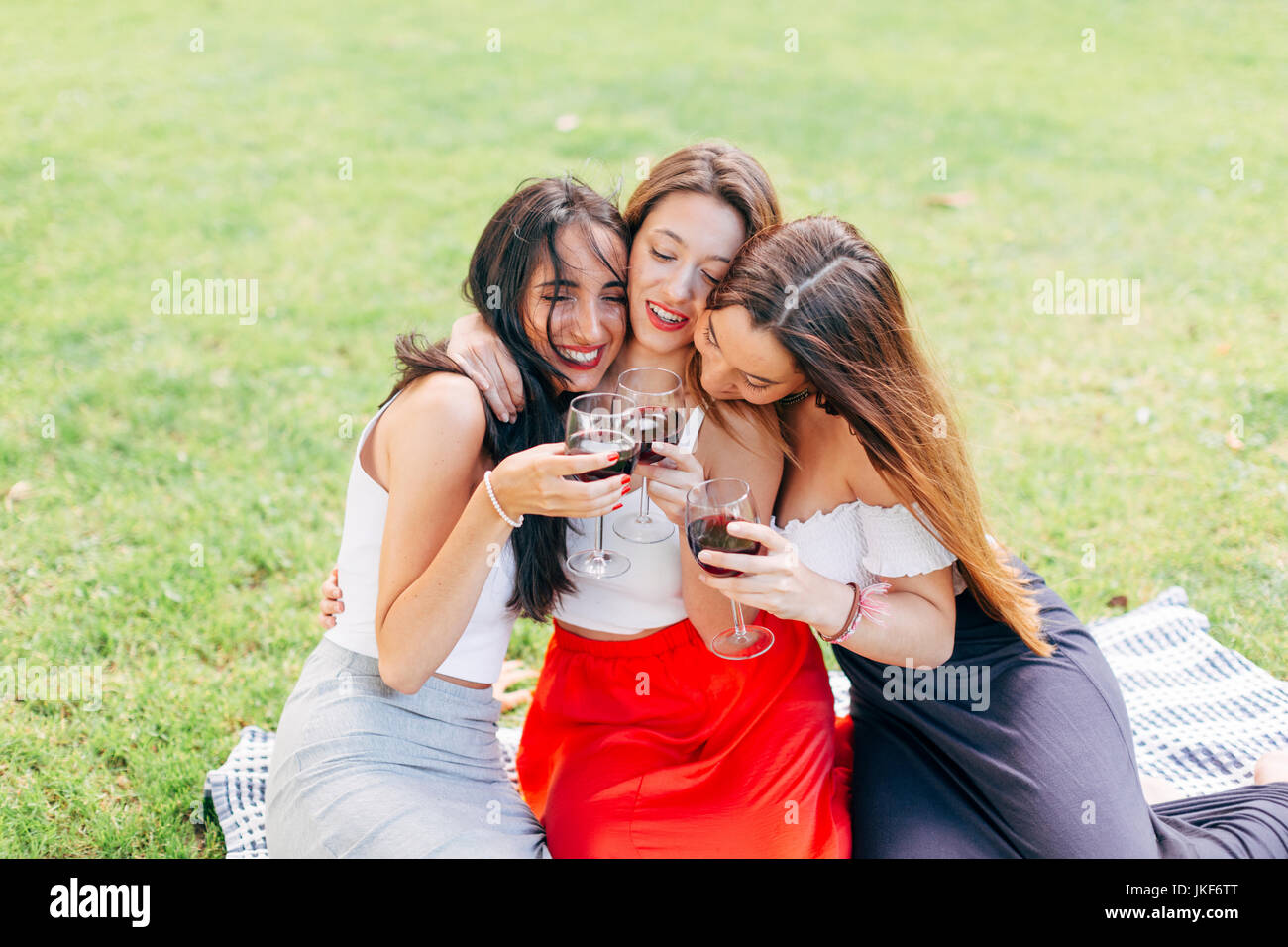 Happy friends in a park hugging and enjoying red wine Stock Photo - Alamy
