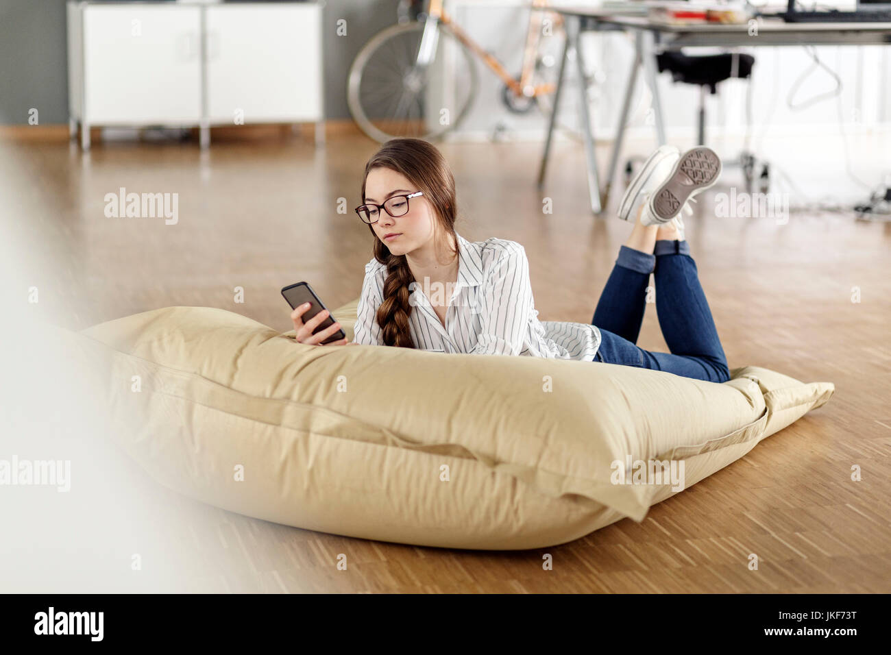 Young woman with cell phone lying in bean bag in office Stock Photo - Alamy