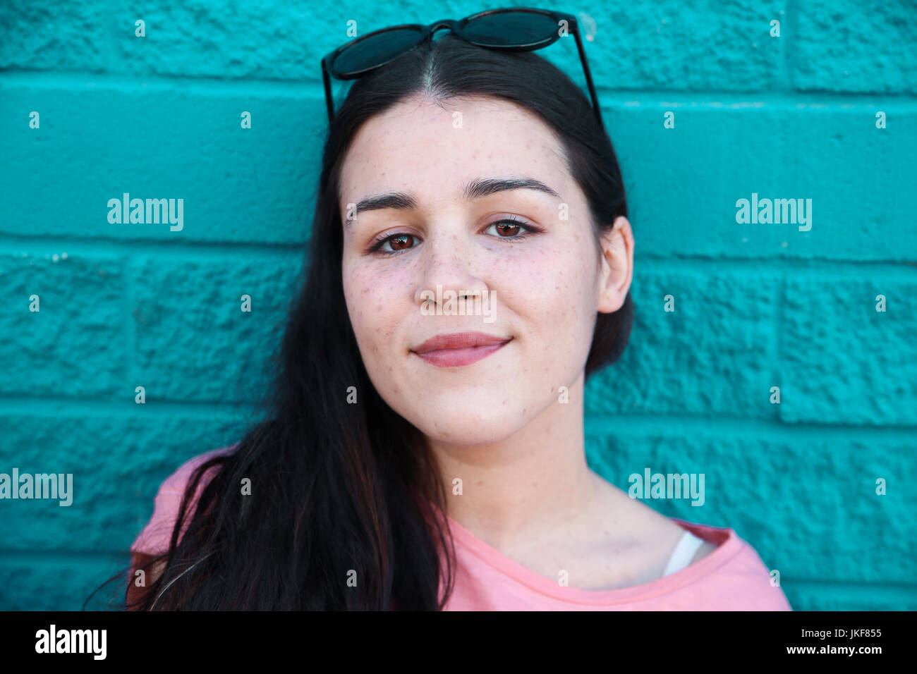 Portrait of smiling young woman in front of blue brick wall Stock Photo ...