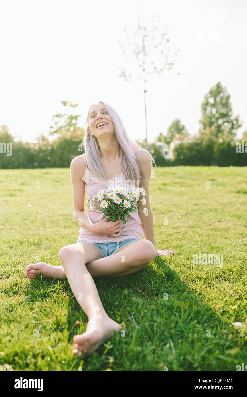 Laughing woman sitting on a meadow holding bunch of daisies Stock Photo ...