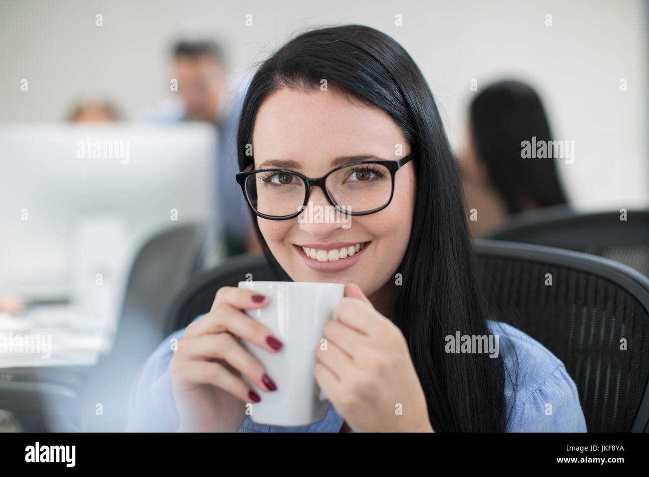 Employee enjoying a cup of coffee at her desk Stock Photo