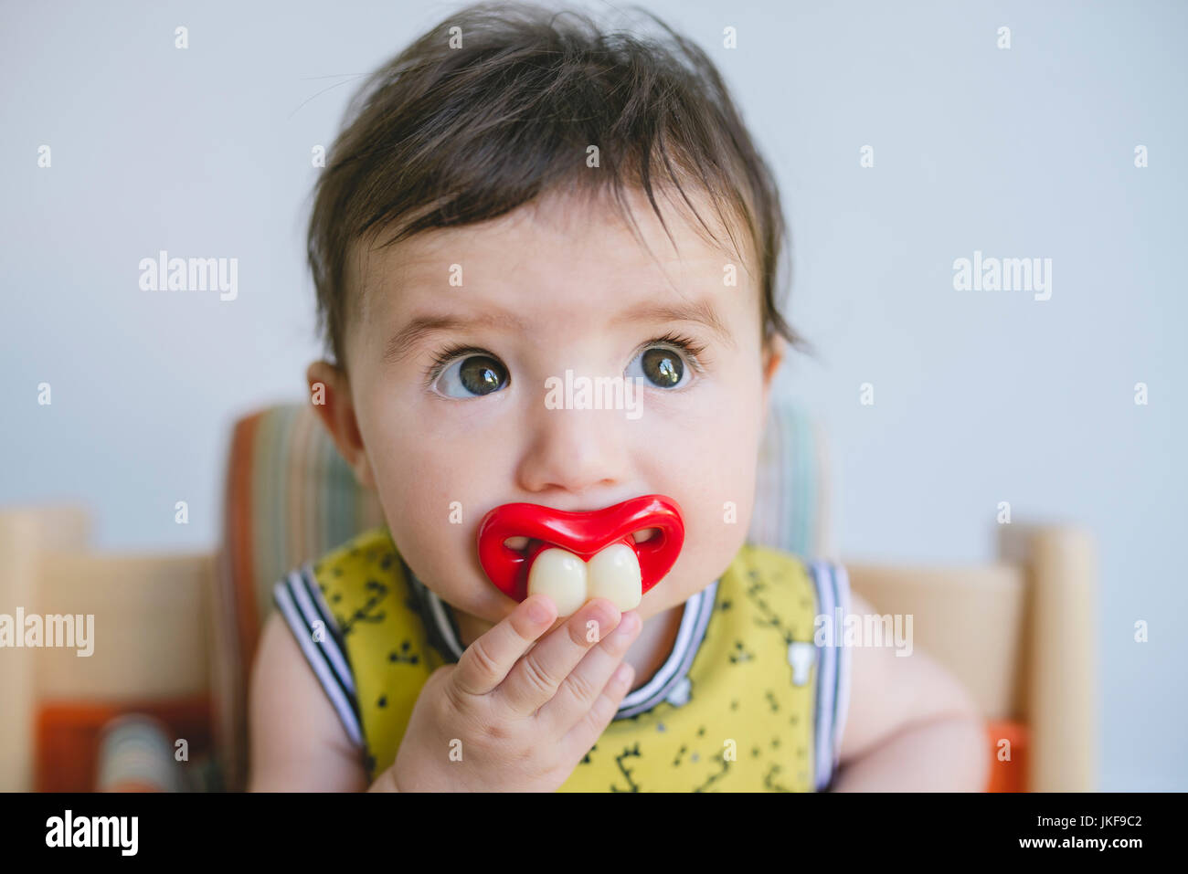 Portrait of baby girl sucking a pacifier with false teeth and mouth Stock Photo