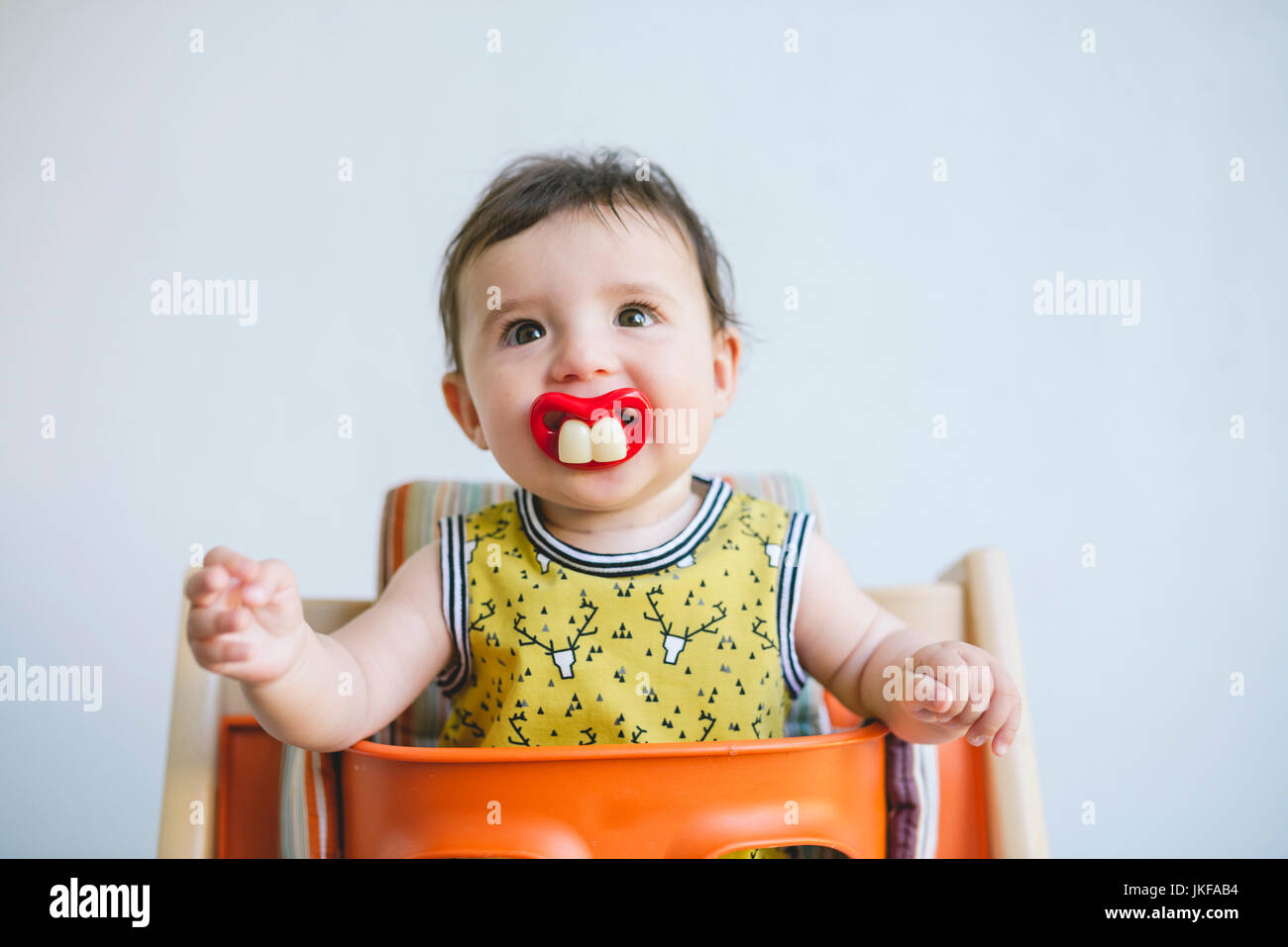 Portrait of baby girl sucking a pacifier with false teeth and mouth Stock Photo