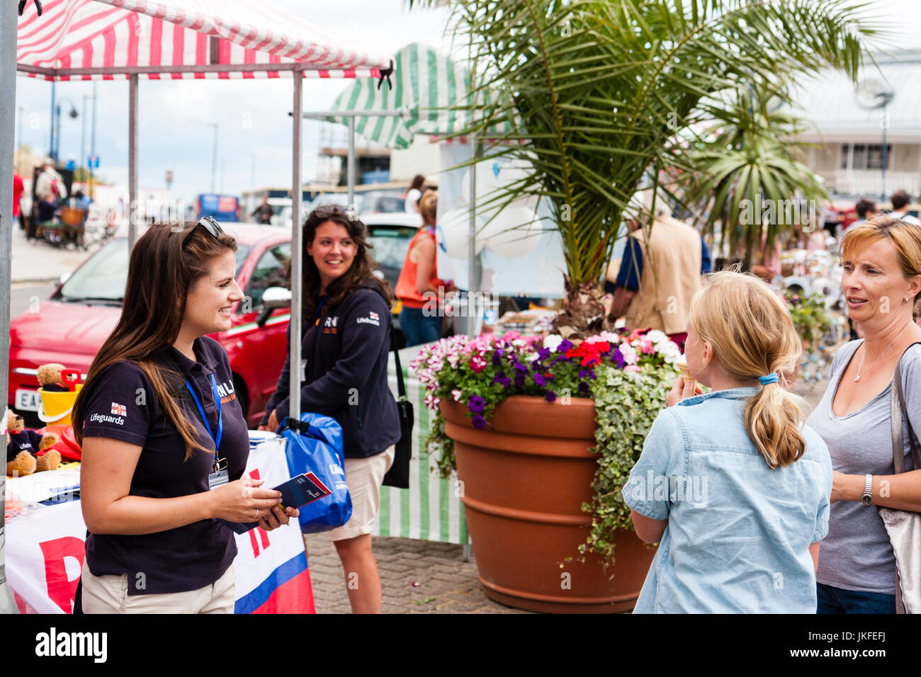 Mother and daughter ask questions to a young woman, 20s, Royal National Lifeboat Fund raiser at an RNLI stall on Ramsgate seafront. Stock Photo