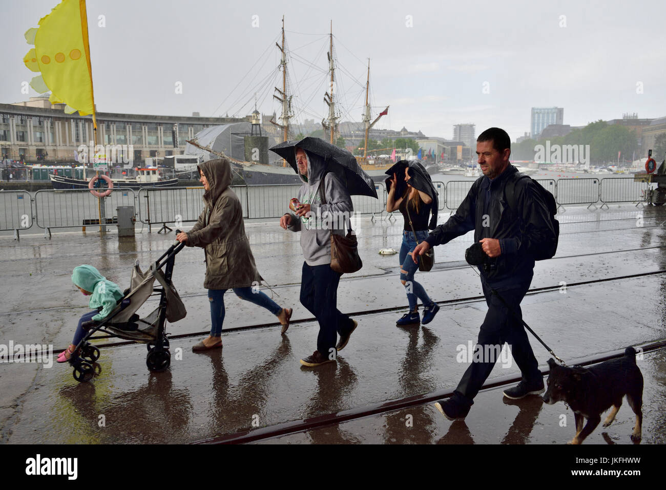 Bristol, UK. 23rd July, 2017. Rather mixed starting with heavy rain before the festival opened at 12:00 which then cleared to mixed sunshine and cloud. By 16:00 the forecasts were correct and a downpour commenced easing off at the official closing time for the festival. People trying to protect themselves from the rain walking along Bristol harbour quayside by M Shed.s. Credit: Charles Stirling/Alamy Live News Stock Photo
