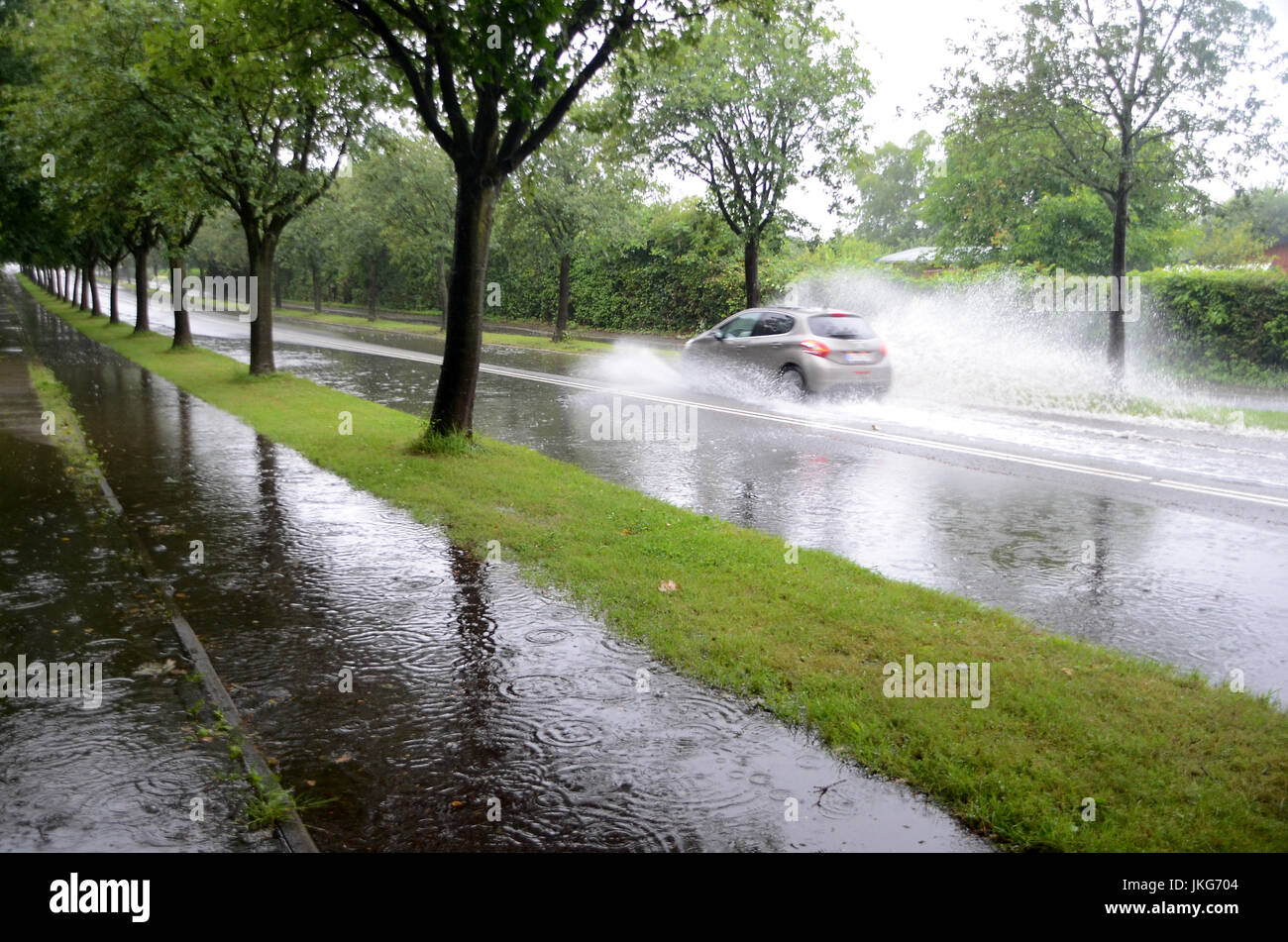 Car splashes trough water on a partly flooded road. Stock Photo