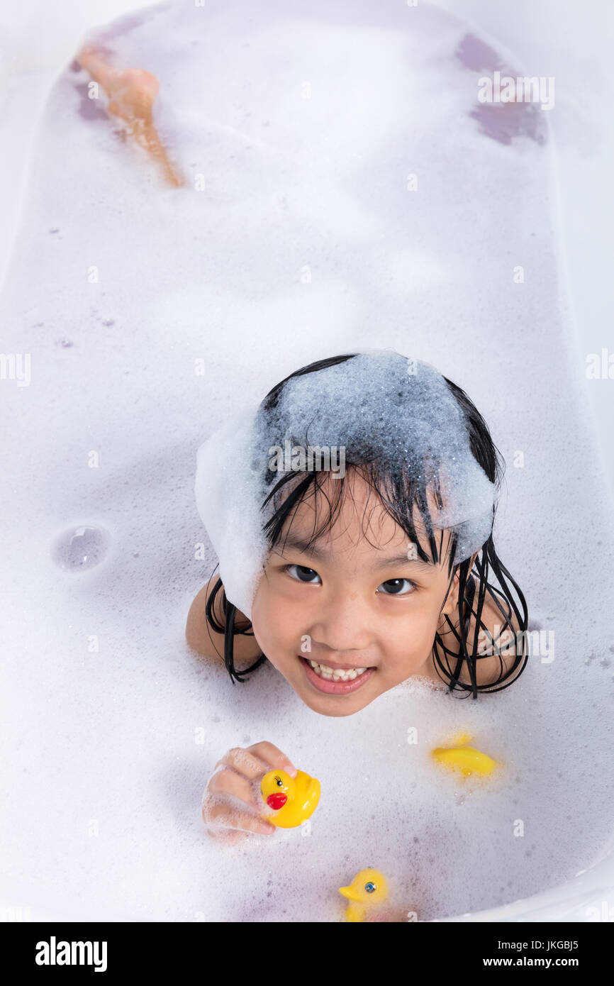 Asian little Chinese girl playing with water and foam in bathtub at