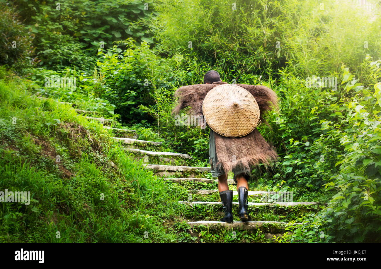 Chinese farmer wearing an antique raincoat walking up stairs Stock Photo