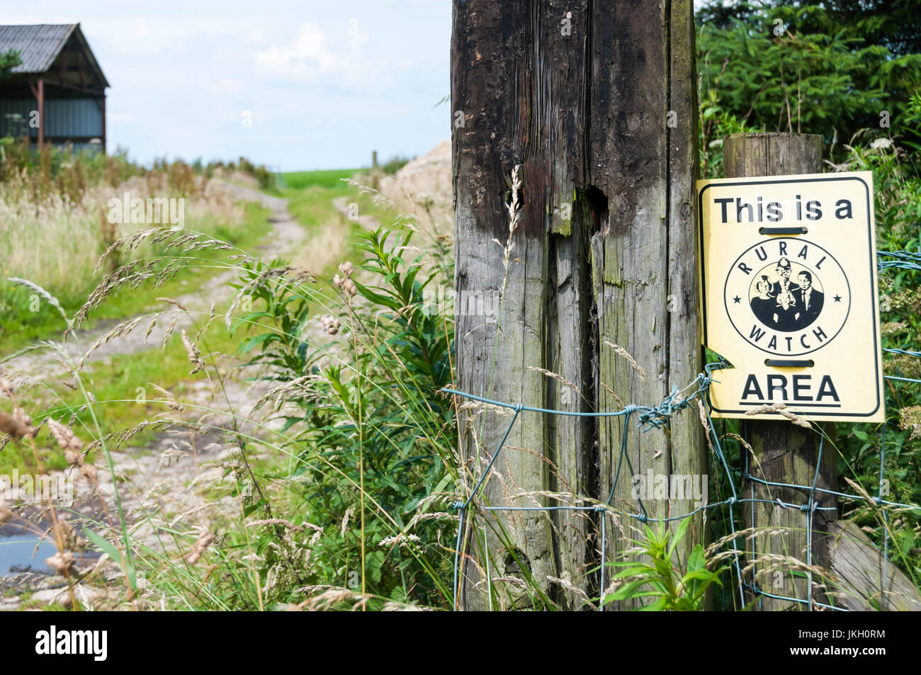A sign beside a quiet farm track reads This is a Rural Watch Area. Stock Photo
