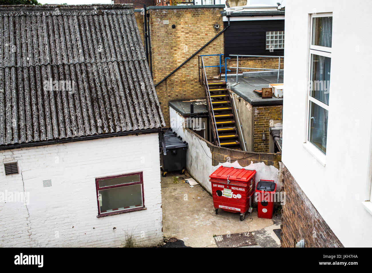 Urban Alleyway with Red Wheely Bins in Disrepair and Brick Buildings with No People Stock Photo