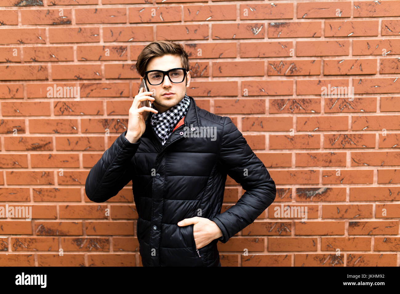 Portrait Of A Young Man Talking On The Phone Over Brick Wall Background portrait-of-a-young-man-talking-on-the-phone-over-brick-wall-background
