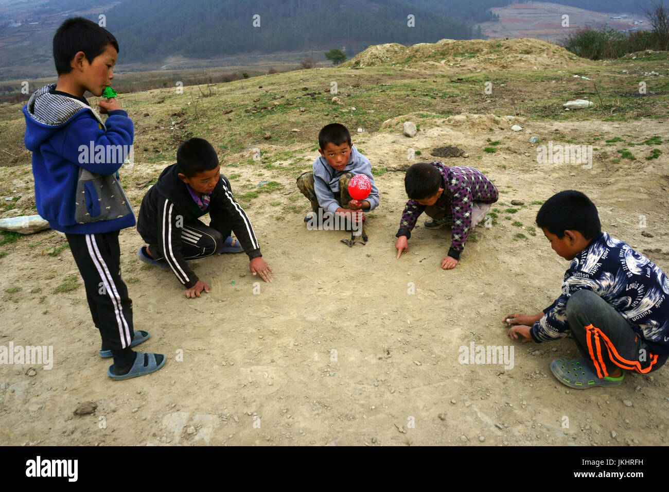 Boys palying game on ground hitting small rocks like marbles, Phobjika valley, Bhutan Stock Photo