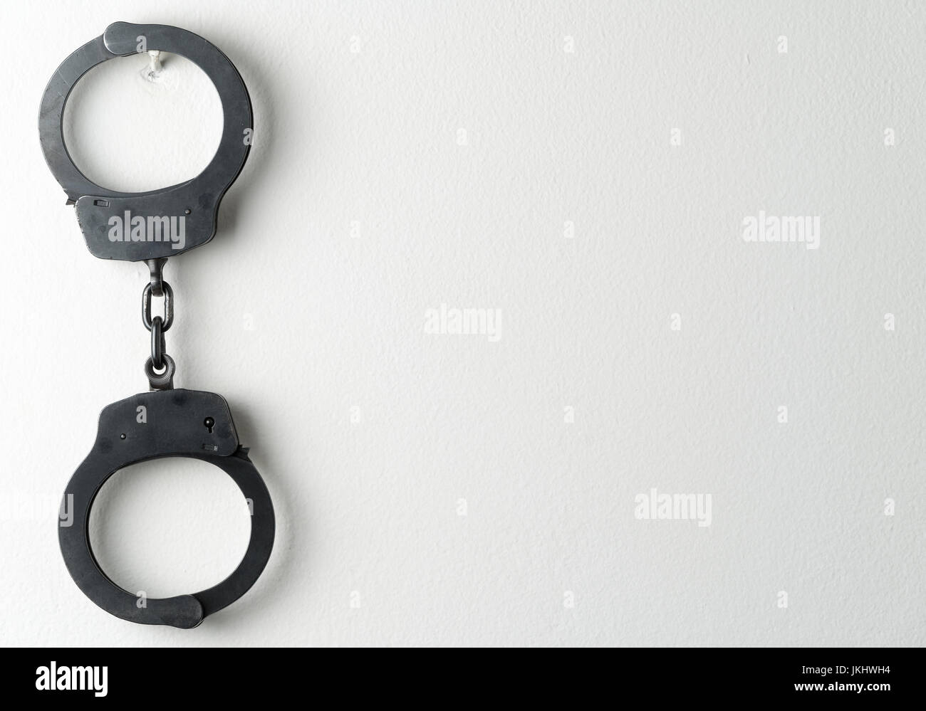Police handcuffs on white painted wall Stock Photo