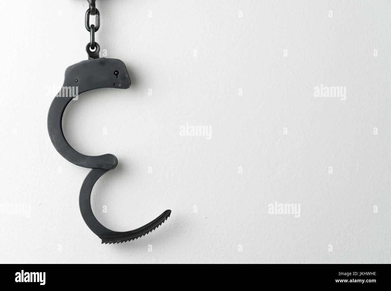 Open police handcuffs on white painted wall Stock Photo