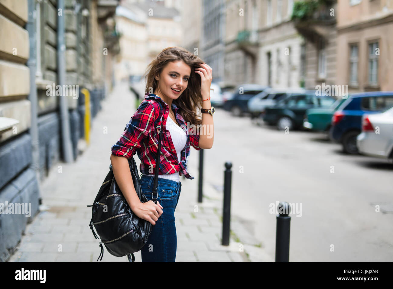 Cheerful attractive young woman with red backpack and book walking in ...