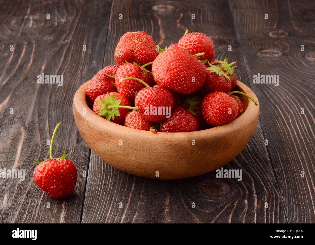 Ripe strawberries in wooden bowl and green leaves on old table, top ...