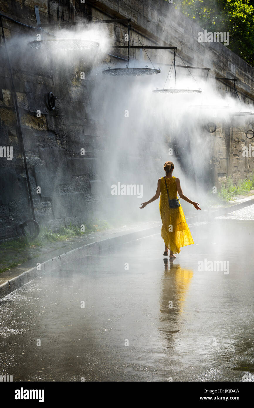 A young women walking with her arms spread in the mist of a public water mister installed on the wharf of the river Seine in the center of Paris. Stock Photo