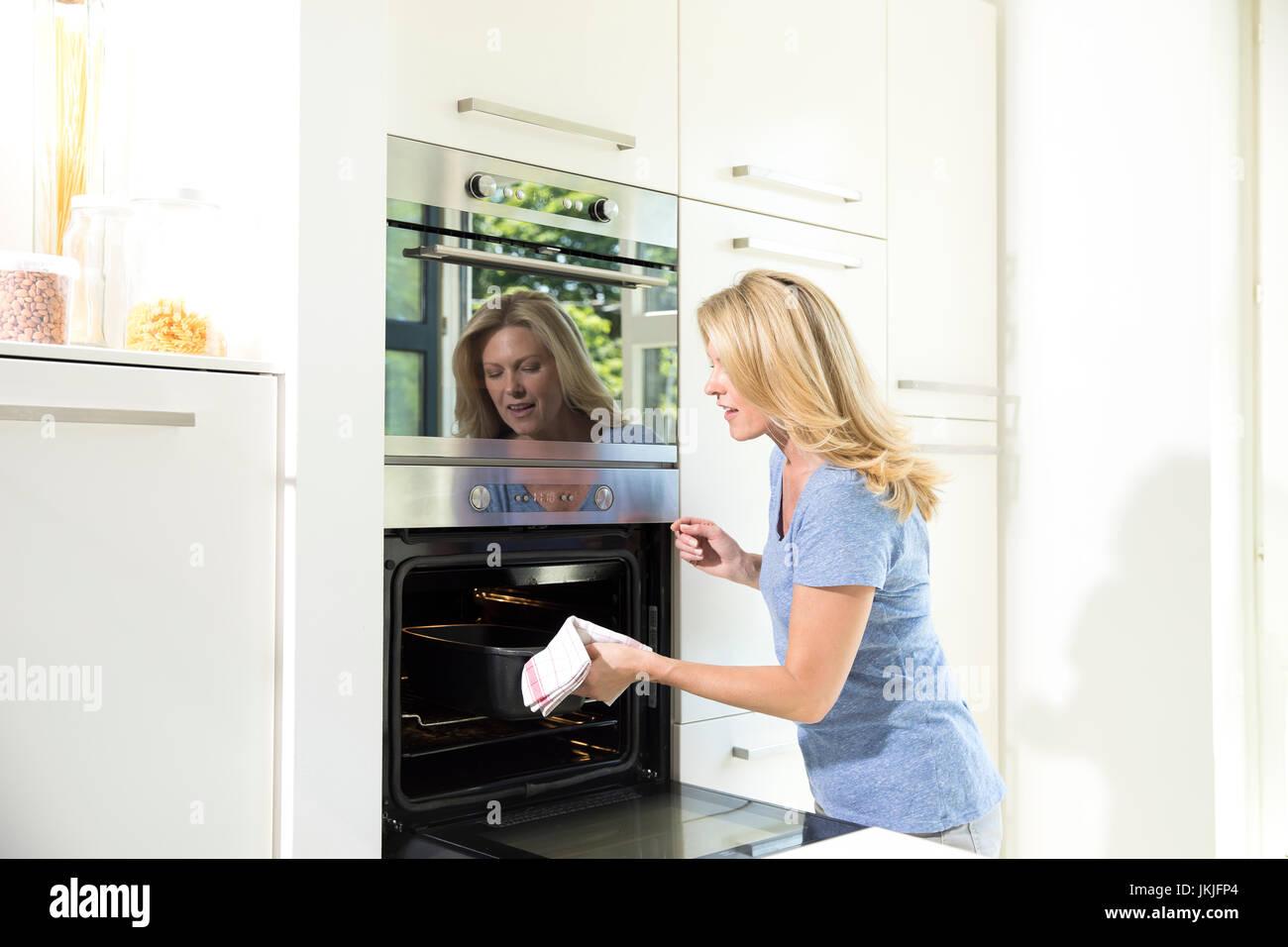 Woman in kitchen taking casserole dish out of oven Stock Photo